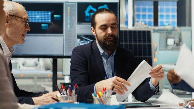 Business executives meet with investors to discuss the integration of automation technology in solar panel production processes, looking over paperwork and schematics, camera B