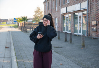 Fototapeta premium Woman experiencing trouble or discomfort while checking her smartphone on a city sidewalk, dealing with a problem, feeling confused, concerned, sad, or looking for something missing