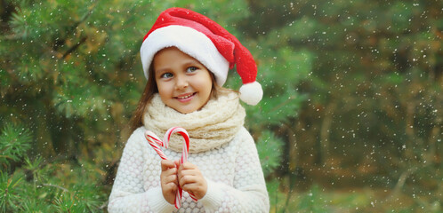 Christmas portrait of happy smiling little girl child in santa red hat with sweet lollipop cane toys