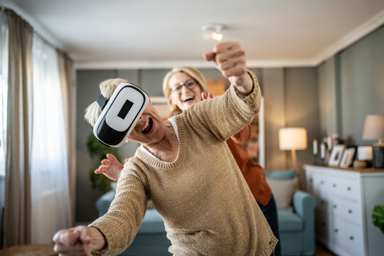 Senior woman playing virtual reality game at home with friend - Powered by Adobe