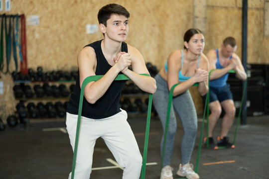 Focused young man training with resistance band for health wellness, strong biceps or abs muscles in gym health center - Powered by Adobe