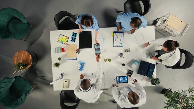 Top down view of medical staff participating in a clinical discussion on diagnosis and treatment. Doctors and nurses analyze healthcare data and coordinate strategies.