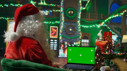 Santa Claus responding to kids requesting gifts, typing on green screen laptop. Person impersonating Santa Claus asking children what they want for Christmas using chroma key notebook, camera A