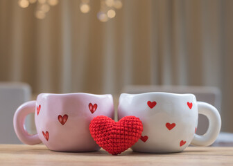 Two cups with hearts and knitted heart on wooden table with blurred beige background for Valentines Day