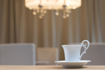 Porcelain coffee cup and saucer on wooden table with blurred beige dining background