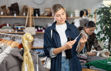 Focused young woman choosing warm gloves for autumn-winter season in modern clothing shop