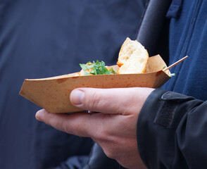 A close-up of a person holding a cardboard tray with fresh street food at an outdoor farmers market Naplavka in Prague.