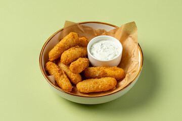 A bowl filled with crunchy, golden-brown snacks sits on a light green surface. Accompanied by a small dish of creamy dipping sauce, these treats offer a perfect blend of flavors