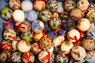 A box packed tightly with colorful hand-painted Christmas baubles and ribbons. A background of Christmas baubles.