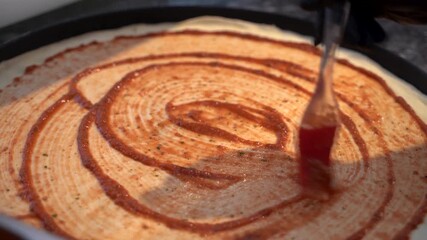Close up of spreading tomato sauce on fresh pizza dough