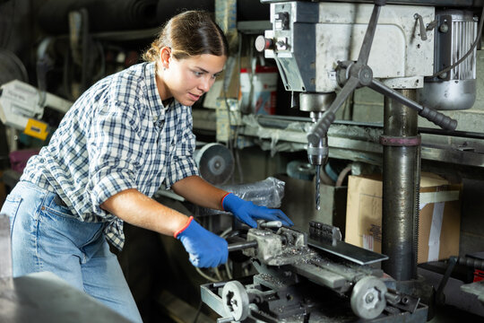 Young woman in uniform works with drill machine in metallurgical workshop