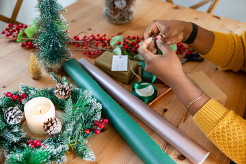 African American woman wrapping holiday gift at home table with wrapping paper, ribbon, copy space