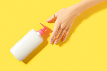 Womans hand holding white bottle on yellow background. Self care concept.