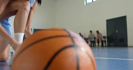 Resting basketball occupying center on blue court, kneeling player tying shoe in light blue uniform