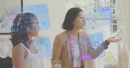 Gesturing Asian designer in tan blazer explaining AR panels at boutique, with pink measuring tape