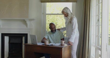 Fototapeta premium Reviewing couple leaning over desk at home in white blouse, green shirt, with laptop and papers