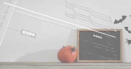 Displaying small orange pumpkin topped with plastic spider on wood table with board, bats, glitch