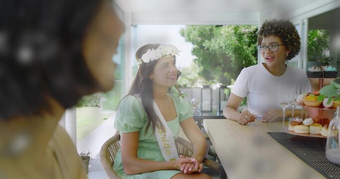 Smiling bride-to-be sitting in sunroom wearing Bride sash and floral crown, with dessert stand - Powered by Adobe