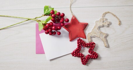 Featuring flat-lay holiday decorations, cards on light wood table, with red berry sprig, red star