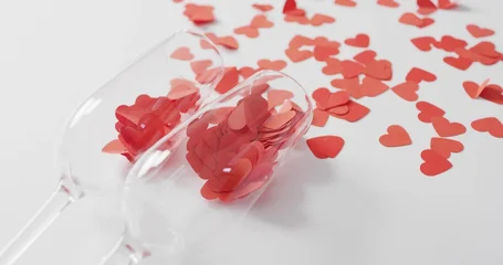 Fotobehang Vlees Tipping two clear stemmed glasses spilling many red heart confetti pieces across white tabletop  © vectorfusionart