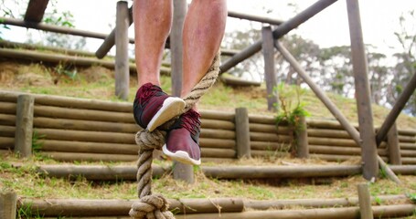 Balancing man legs and feet wrapping around braided rope on terraced log bank with maroon sneakers