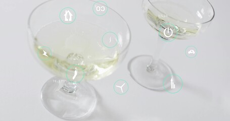 Displaying two coupe glasses holding pale yellow liquid on white tabletop, with teal UI icons © vectorfusionart