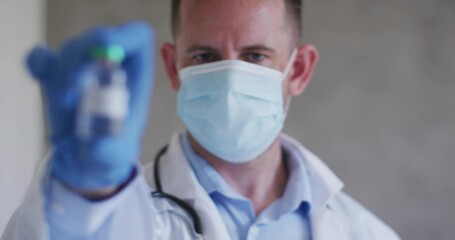 Offering doctor in lab coat, surgical mask holding vial at clinic with blue gloves, stethoscope