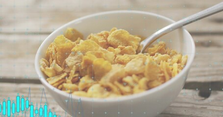 Showing white bowl holding golden cornflakes with spoon resting on kitchen table, turquoise overlay