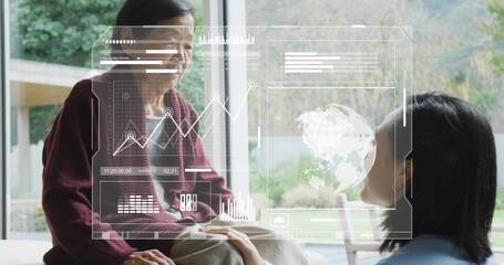 Holding hands adult in blue top and senior in maroon cardigan by window, viewing holographic charts