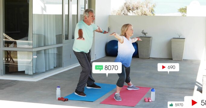 Practicing senior couple holding forward stance on covered patio in workout with mats, social icons
