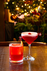 two Christmas themed cocktails on a table with a blurred Christmas tree in the background