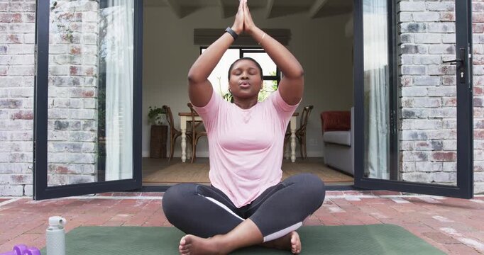 After prayer, African American woman guiding breathing exercise for calm on yoga mat on brick patio