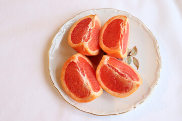 Close-up of cut grapefruit on a white vintage plate and a white background. Fruit and good nutrition. Grapefruit and sources of vitamins. Grapefruit background and natural food.