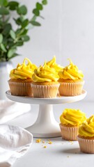Sweet cupcakes, yellow frosting on white stand, with greenery detail