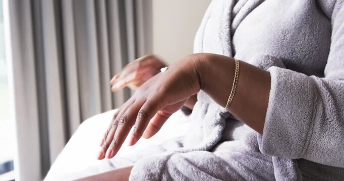 woman lifting bottle pressing pump dispensing lotion rubbing skin on bed grey drapes for hydration