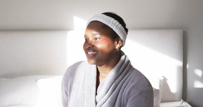 African American woman sitting on bed with eye patches smiling and looking with sunlight streaming