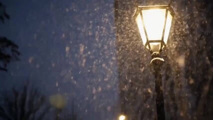 Peaceful winter night snowfall illuminated by warm glowing street lamp, tranquil snowy evening atmosphere with gentle falling snowflakes in quiet seasonal outdoor scene - Powered by Adobe