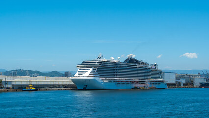 Obraz premium Majestic white cruise ship docked in a sunny port against a clear blue sky, emphasizing travel, luxury, and maritime transport