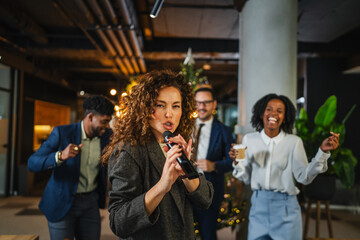 Coworkers singing karaoke celebrating christmas party in office