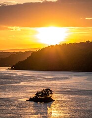 Sun setting over an island with trees on a calm, golden-hued lake