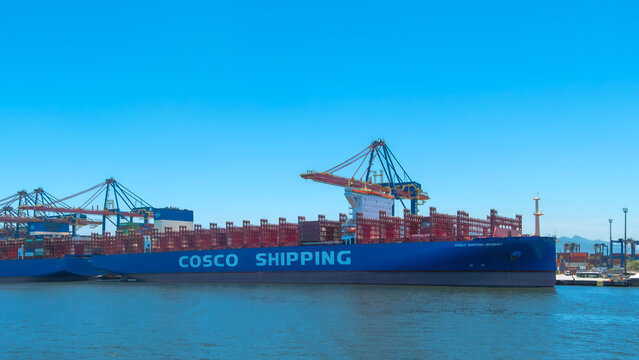 Massive blue COSCO SHIPPING container ship, ready for loading, docks under large port cranes