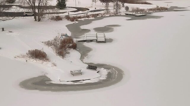 4K Aerial View of a Frozen Suburban Lake Shoreline with Snow-Covered Docks and Benches in Orland Park, Illinois