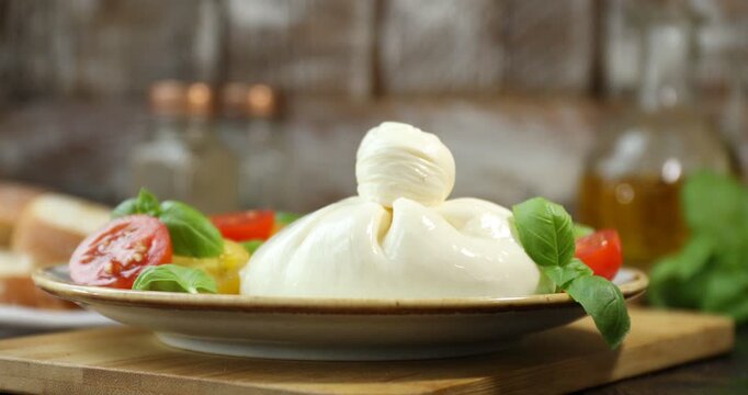 Woman putting basil onto delicious burrata cheese and tomatoes at wooden table, closeup