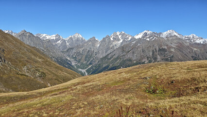 Vast, rugged mountainous landscape of the Svaneti region in Georgia, showcasing high alpine meadows leading toward the snow-dusted, rocky peaks of the Greater Caucasus