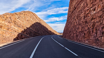 Desert Highway Surrounded by Towering Red Rock Formations Under a Dramatic Blue Sky