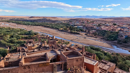 Elevated panoramic view of the historic A&iuml;t Benhaddou ksar and kasbah in Ouarzazate, Morocco, showing the surrounding arid valley, riverbed, and palm oasis