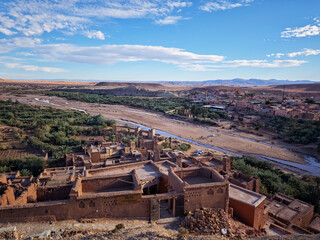 Elevated panoramic view of the historic A&iuml;t Benhaddou ksar and kasbah in Ouarzazate, Morocco, showing the surrounding arid valley, riverbed, and palm oasis