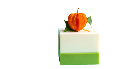 A small, cube-shaped confection, green base, white middle, decorated with orange paper-like plant