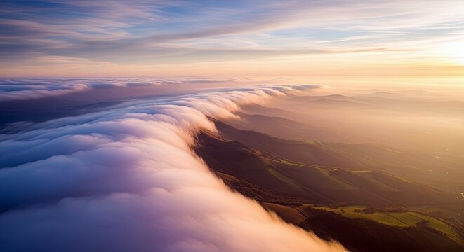 Aerial view of clouds cascading over mountain ridges at sunset, creating a dramatic and ethereal landscape.