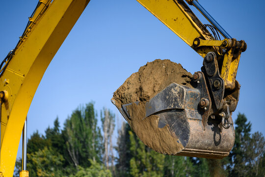Closeup of excavator bucker full of dirt overhead against a sunny blue sky, earthworks construction project site on a sunny day
